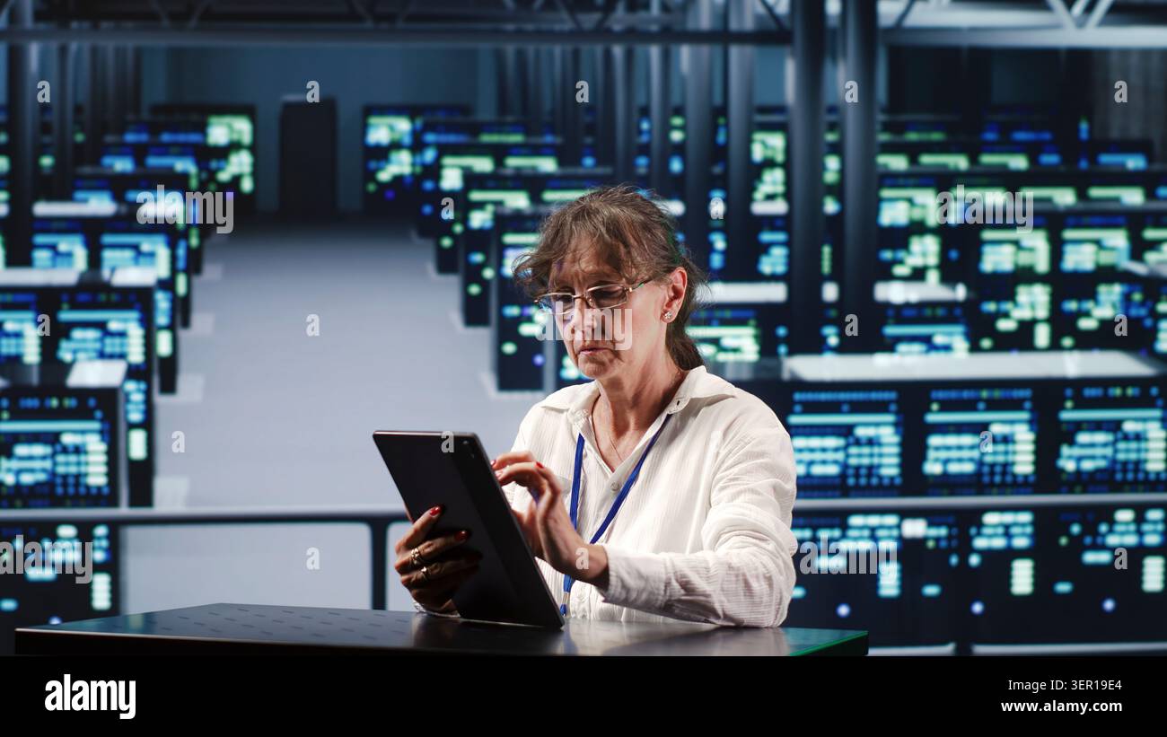 Competent manager in data center housing high-end devices capable of quickly and efficiently performing complex computations and data analysis, using tablet to fix issues. Stock Photo