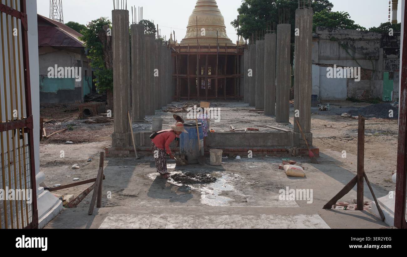 Woman working at new entrance at Eain Daw Yar Pagoda on 88th Street, with children nearby, concrete pillars, and golden stupa in background. Stock Photo