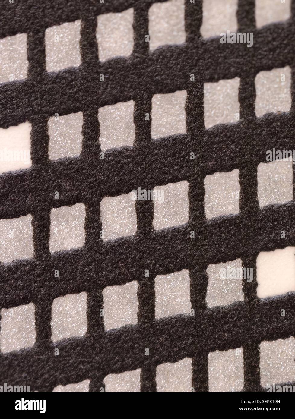 Macro view of a patterned surface showing a black felt-like grid with regularly spaced white granular square inserts. Soft diffuse lighting highlights Stock Photo