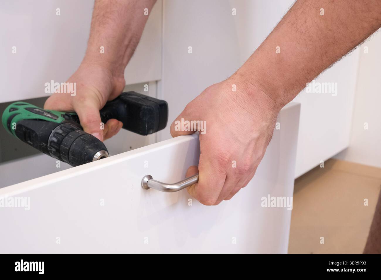 Man installing metal handle on white kitchen drawer Stock Photo
