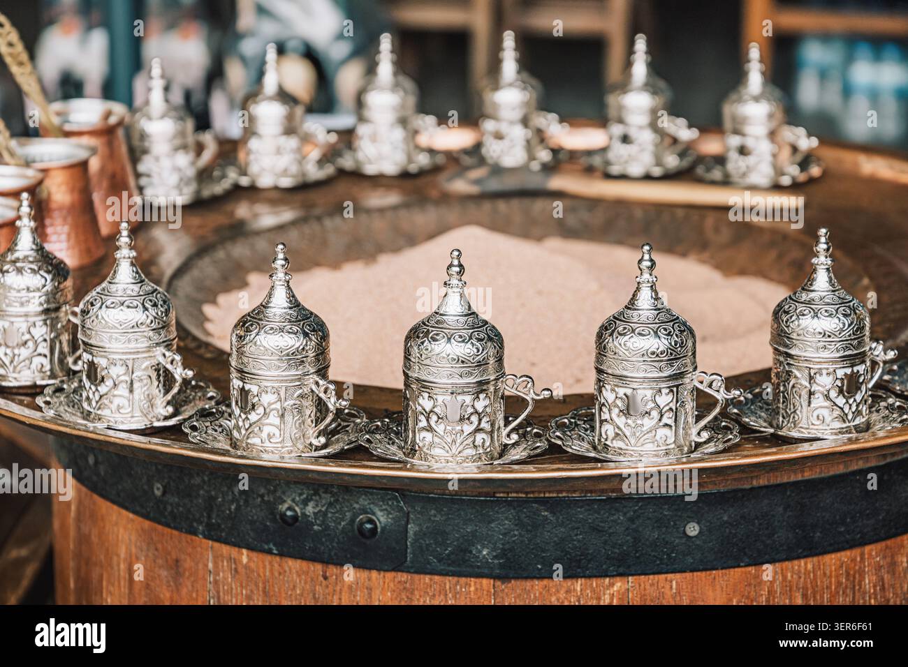 Ornate silver cups and Cezves on a vintage barrel, preparing fresh Turkish coffee in sand. Heritage and culture Stock Photo