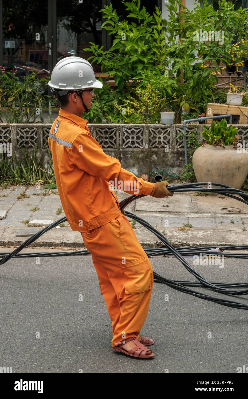 Utility Worker in Orange Uniform Pulling Heavy Black Electrical Cables Stock Photo