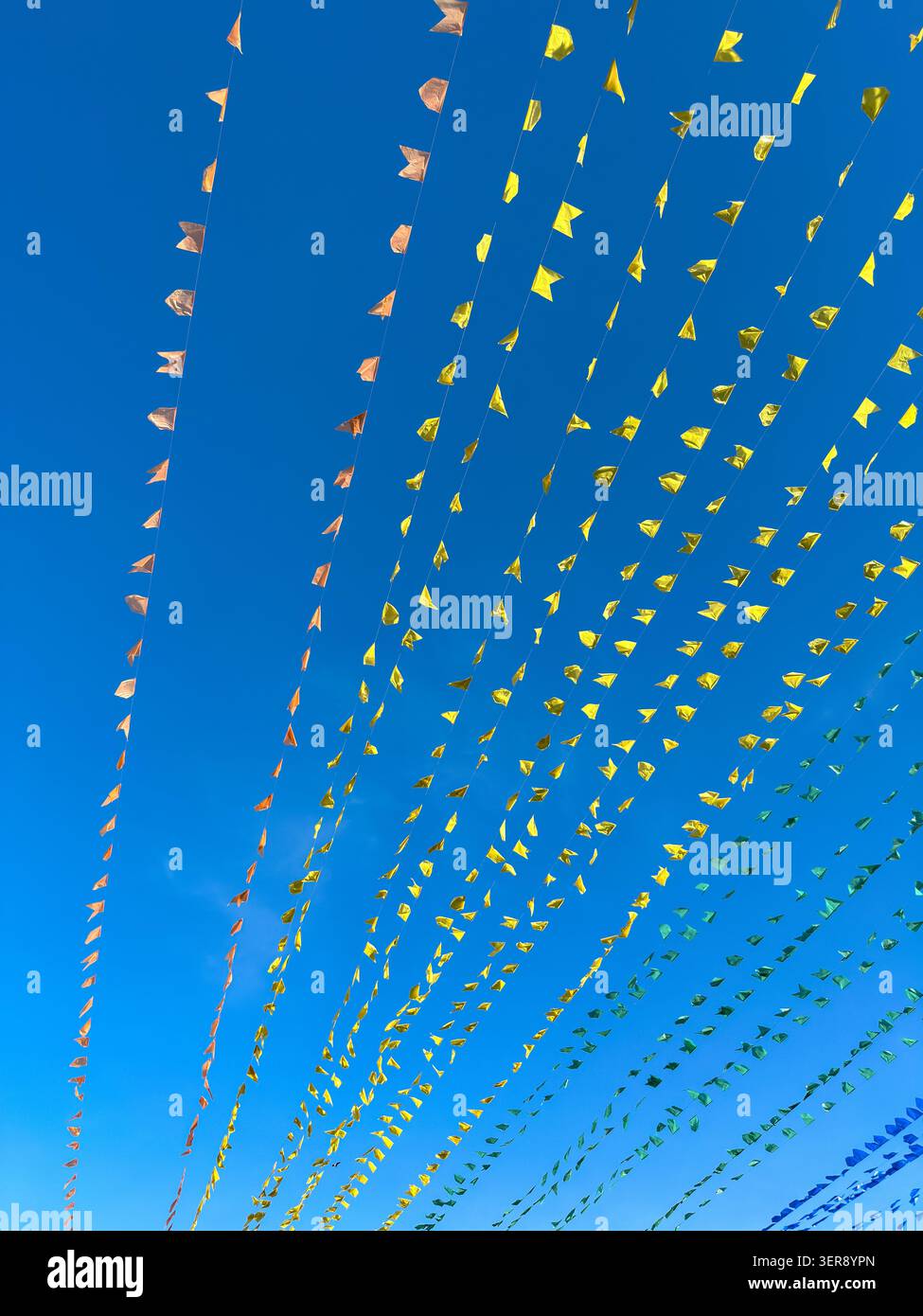 Brightly colored small triangular flags stretch across clear blue sky on strings. Natural light illuminates the celebratory decorations, suggesting ou Stock Photo