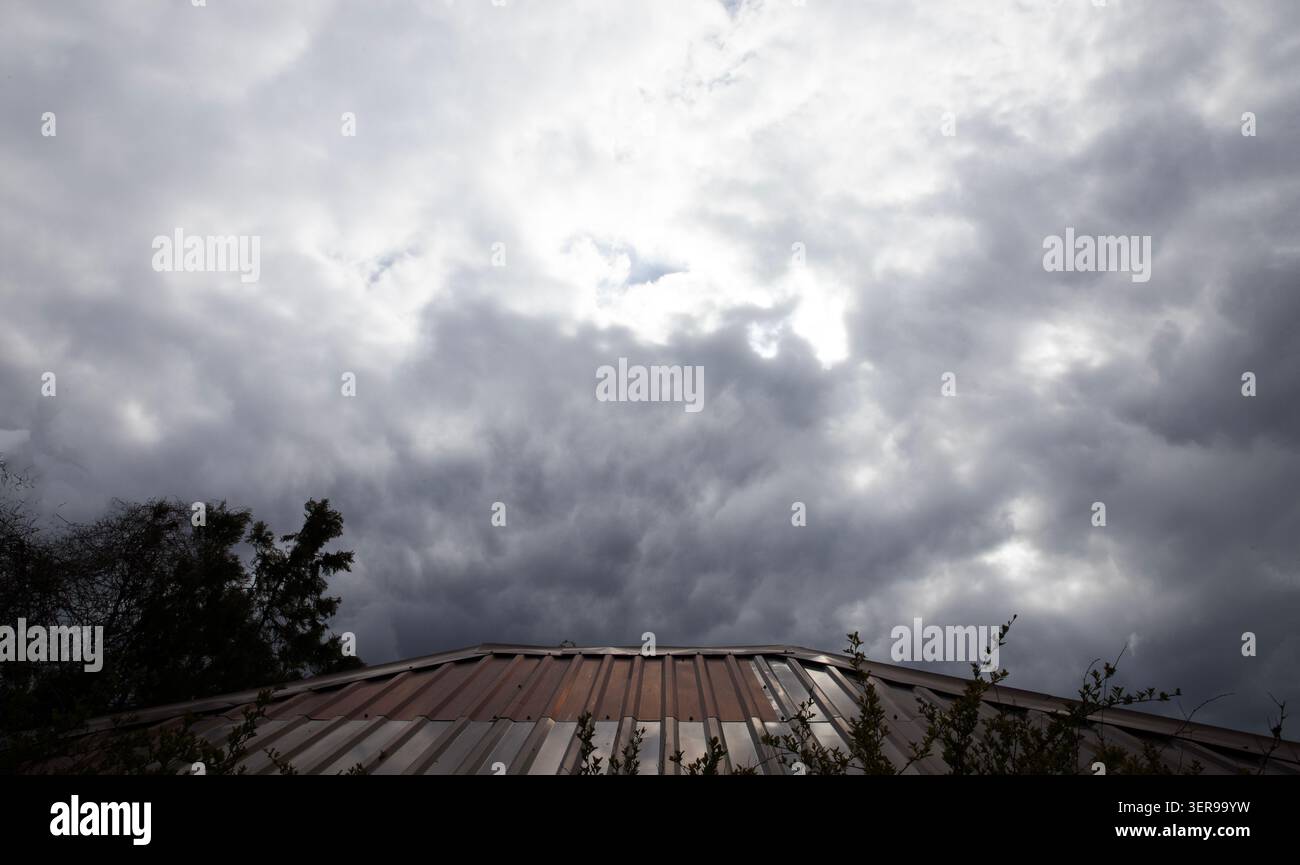 Dark dramatic storm clouds gathering over rooftop before heavy rain begins Stock Photo