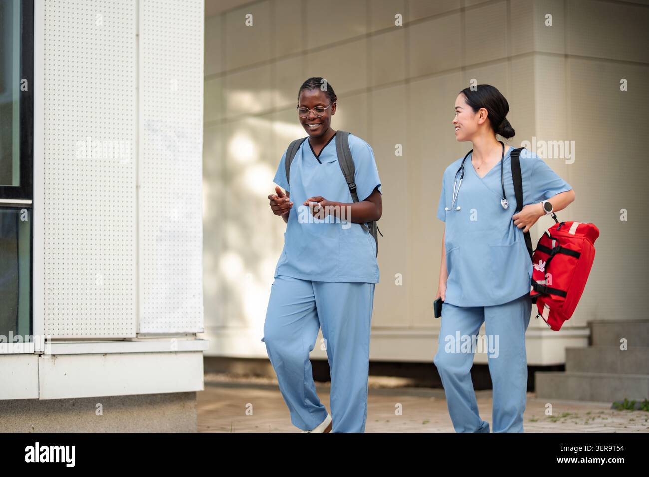 Diverse medical students walking and talking outdoors on campus Stock Photo