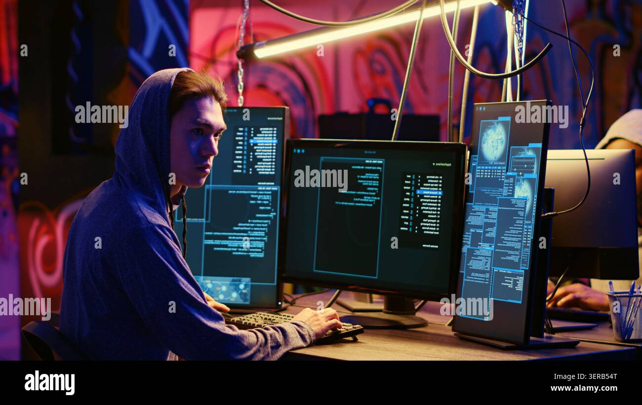 Rogue programmer in graffiti sprayed hideaway targeting vulnerable unpatched connections, focused on getting past digital devices security and stealing valuable sensitive data. Stock Photo