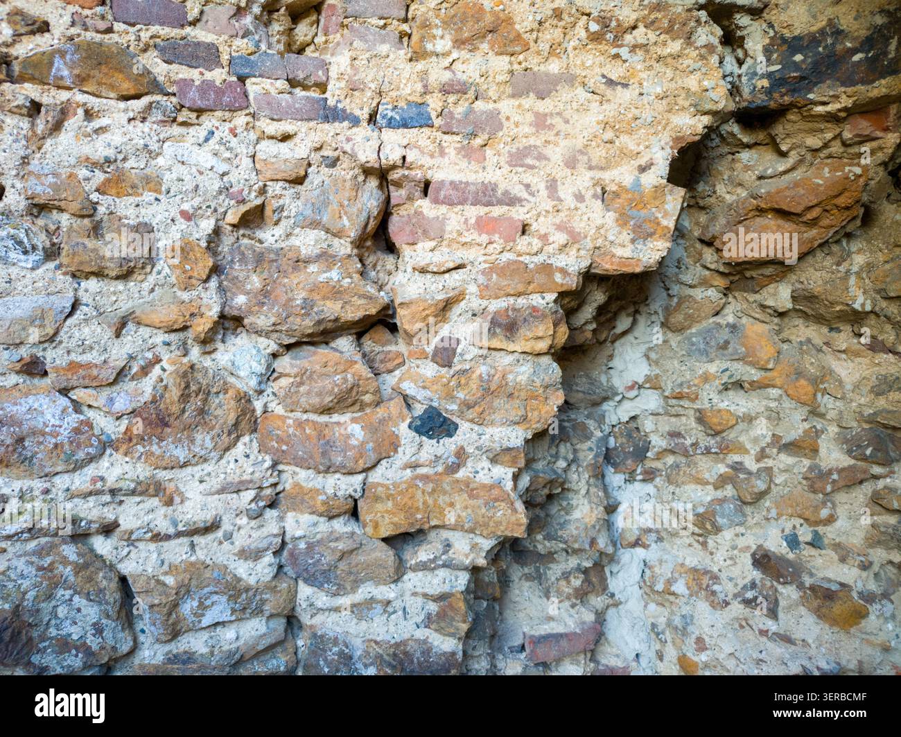 Full frame texture of an ancient weathered wall made of mixed stone bricks and mortar layers. Stock Photo