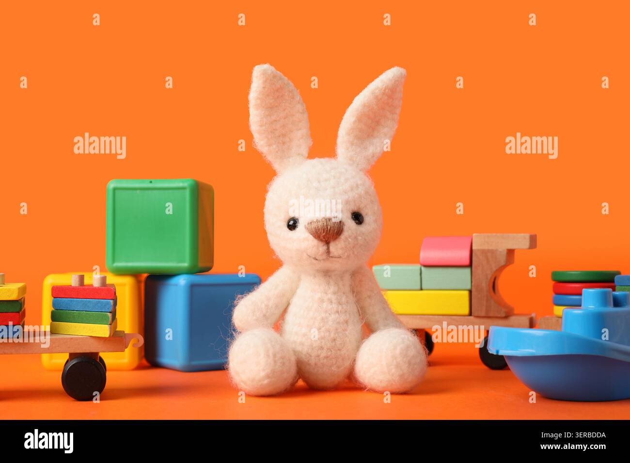 Adorable white knitted bunny toy with colorful wooden and plastic blocks on bright orange background, childhood play and early learning development Stock Photo