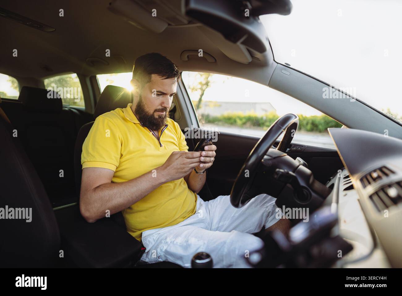 Young bearded man using smartphone while sitting in car driver seat Stock Photo