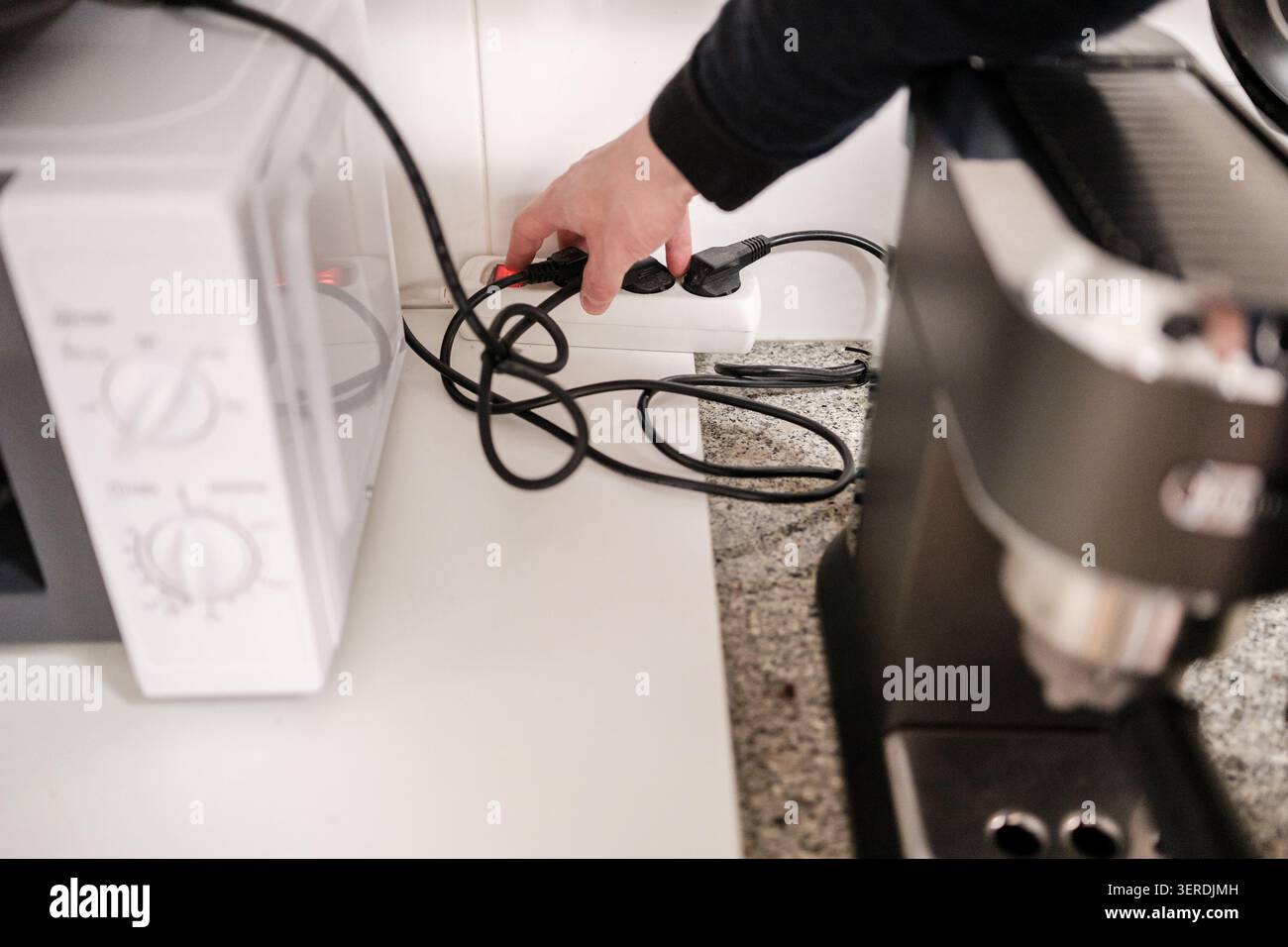 Person powering off a multi-socket adapter for energy conservation in a kitchen Stock Photo