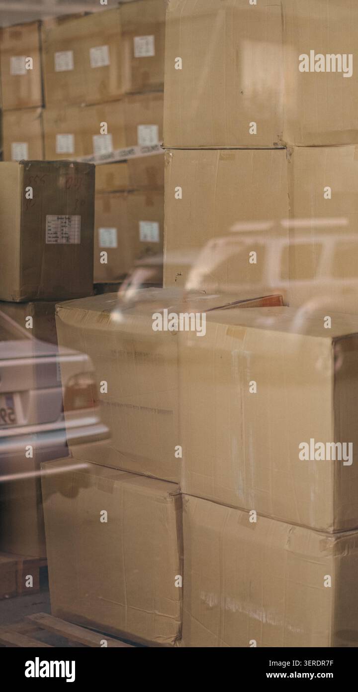 Cardboard boxes stacked inside warehouse behind reflection window close up. Stock Photo