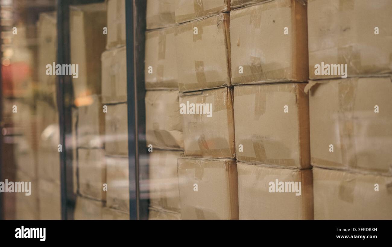 Cardboard boxes stacked inside distribution warehouse behind glass window close up. Stock Photo
