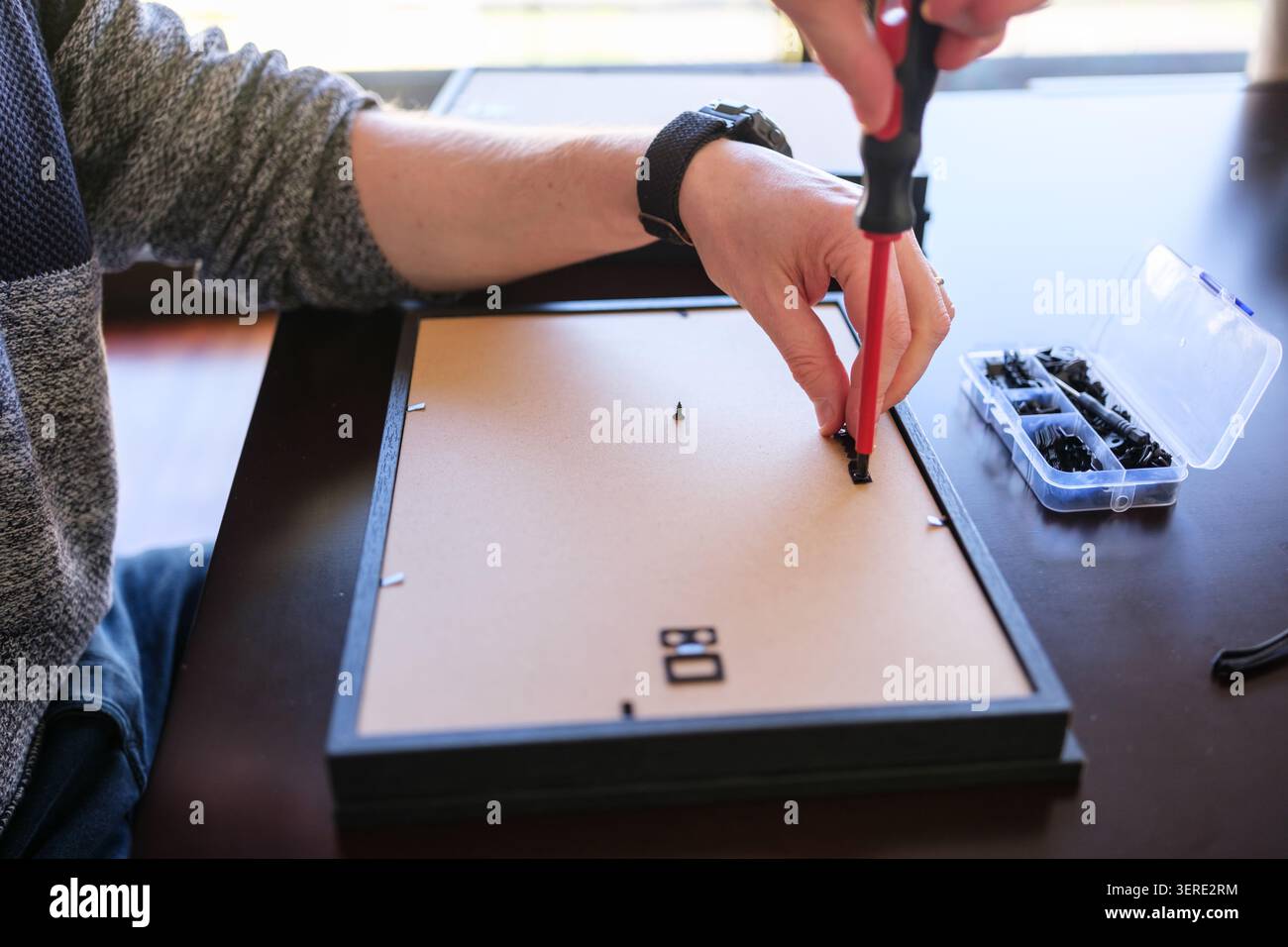 Person's hands assembling a picture frame using a screwdriver and small clips Stock Photo