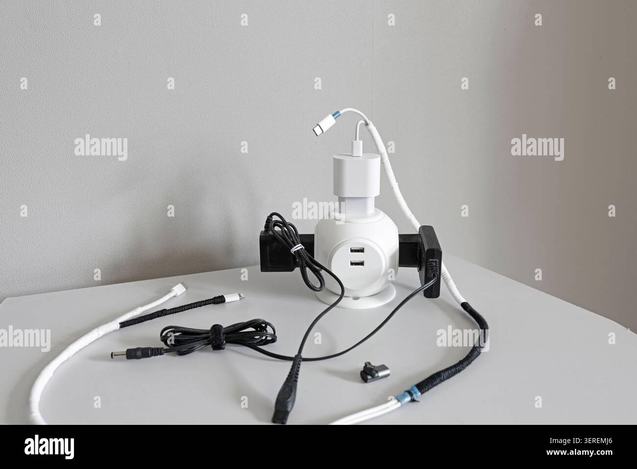 White desktop power cube hub with black adapters and multiple usb charging cables. Tech clutter mess problem on table inside modern minimalist studio Stock Photo