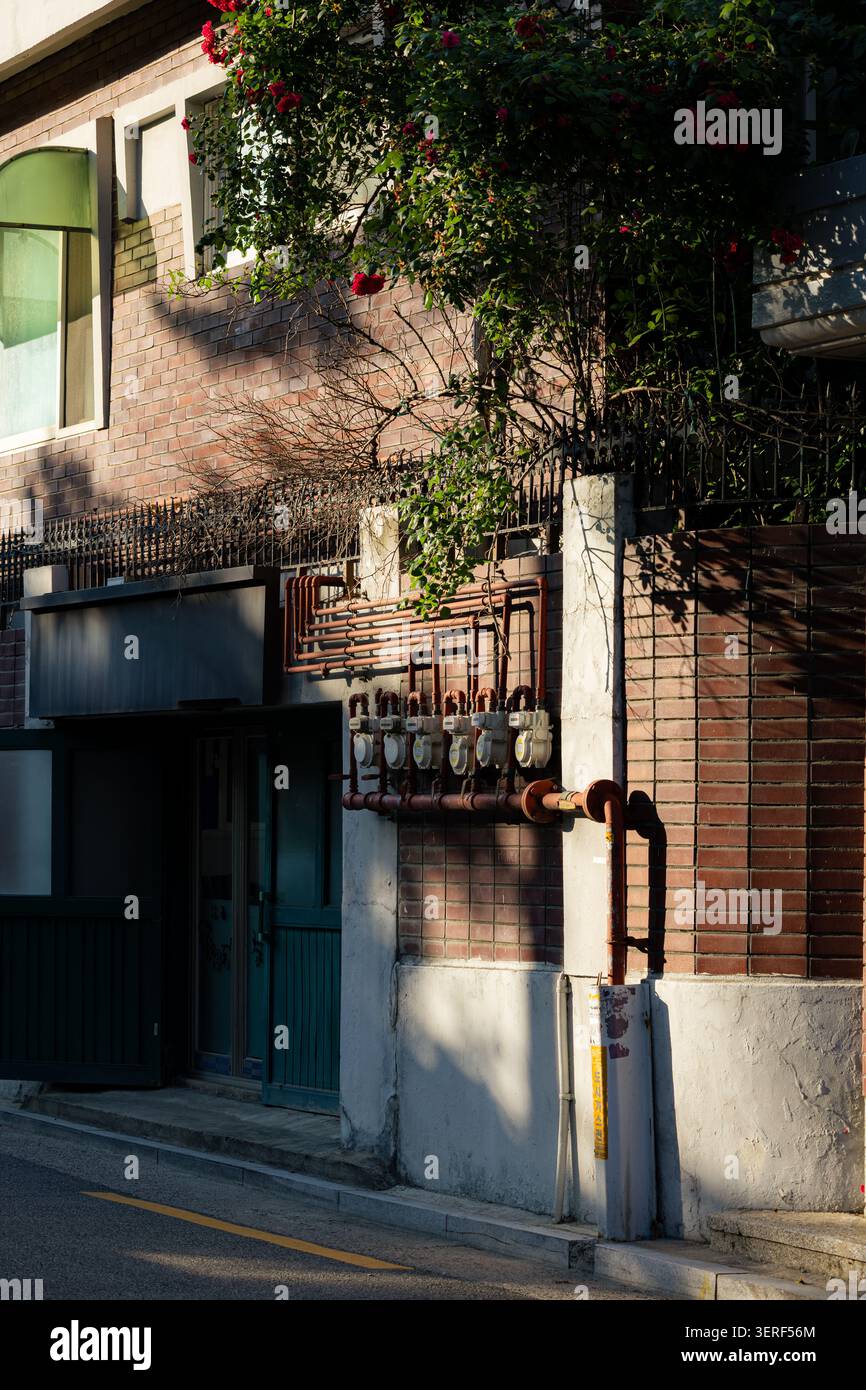 Vintage Korean alleyway with an old red brick wall and gas meters bathed in warm sunlight Stock Photo