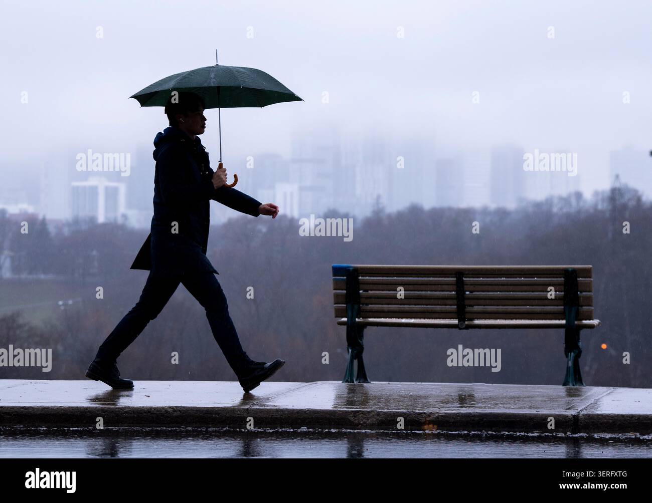 the-toronto-skyline-sits-shrouded-in-fog-as-a-man-walks-in-the-rain-on