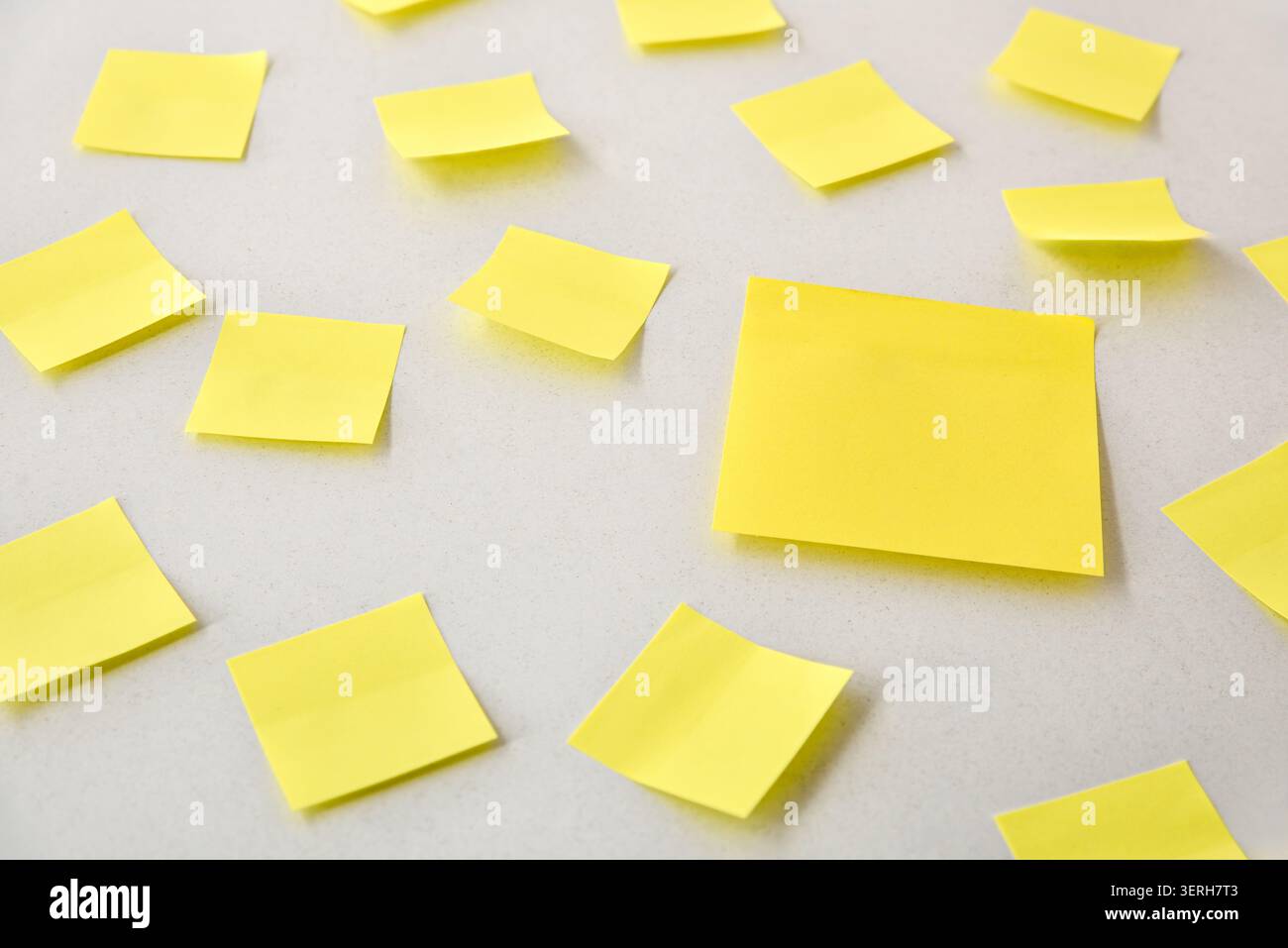 Multiple yellow sticky notes scattered across a clean white surface, creating a minimal office organization and brainstorming concept with ample copy Stock Photo