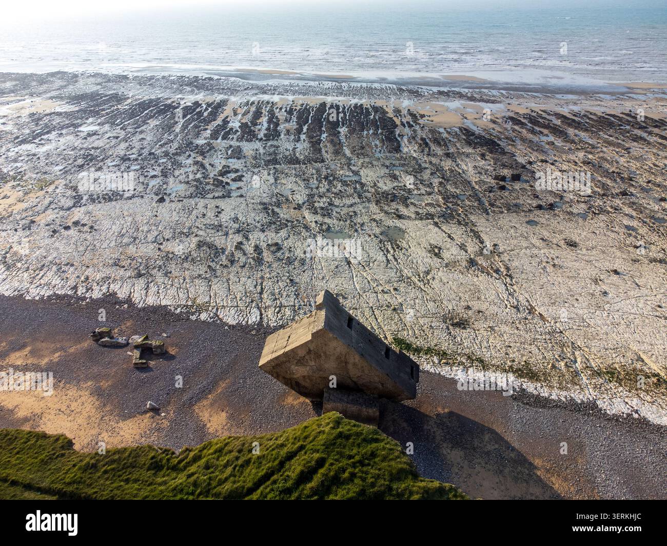 A spectacular aerial view from the cliff edge shows the tilted German bunker on the beach, while the low tide reveals a vast and striking white chalk Stock Photo