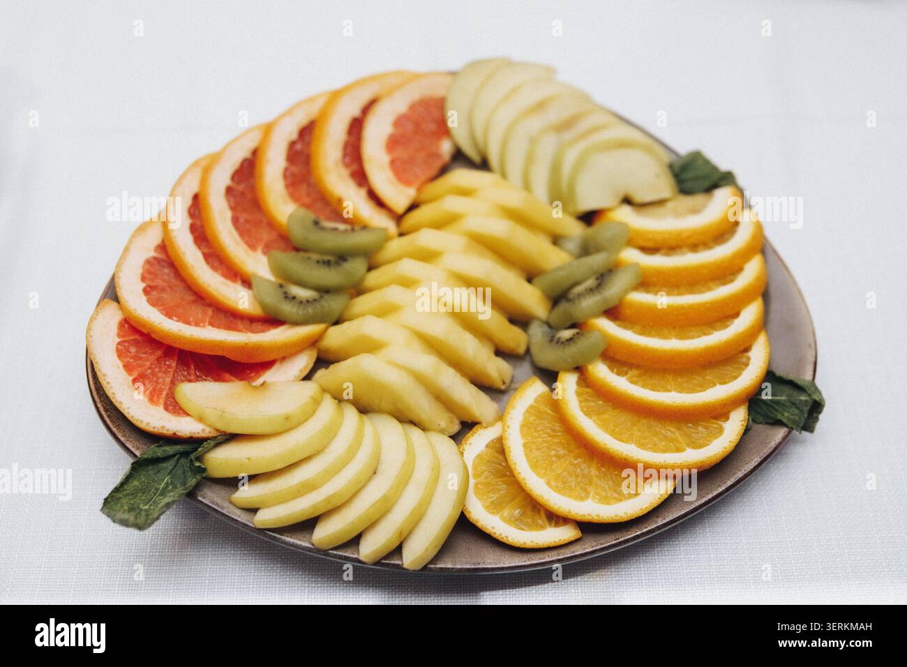 Freshly sliced fruit arranged in concentric circles on a round plate. Bright oranges, apples, and grapefruit create a vibrant display. Green kiwi slic Stock Photo
