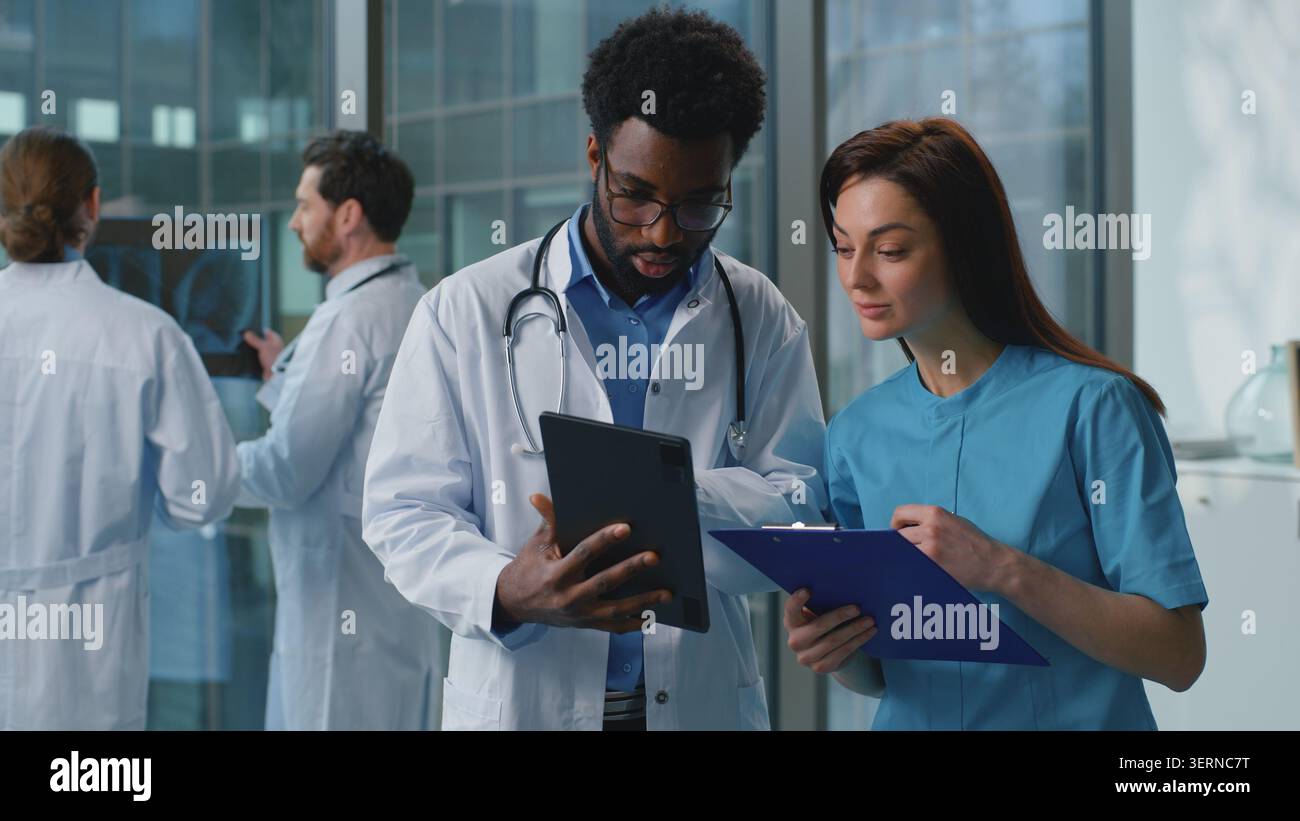 Two diversity doctors man with woman discussing medical examination using digital tablet together in hospital. Caucasian female therapist doctor Stock Photo