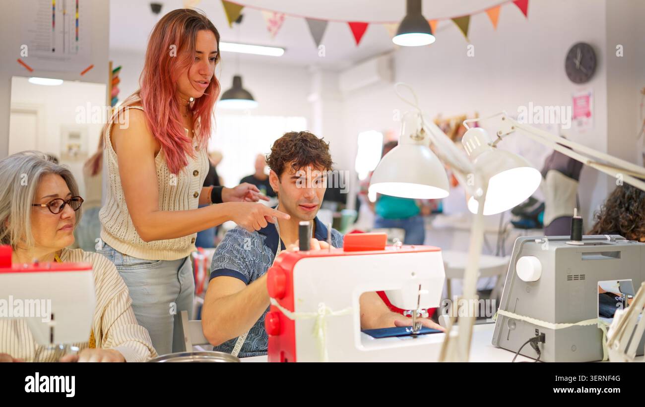 Teacher guiding young man learning sewing machine in workshop Stock Photo