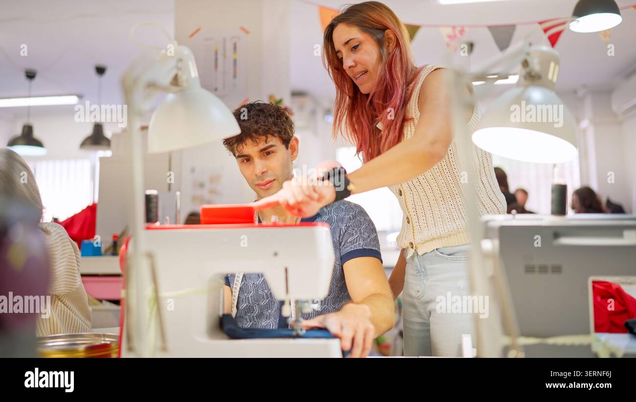Instructor teaching young man sewing machine operation in workshop Stock Photo