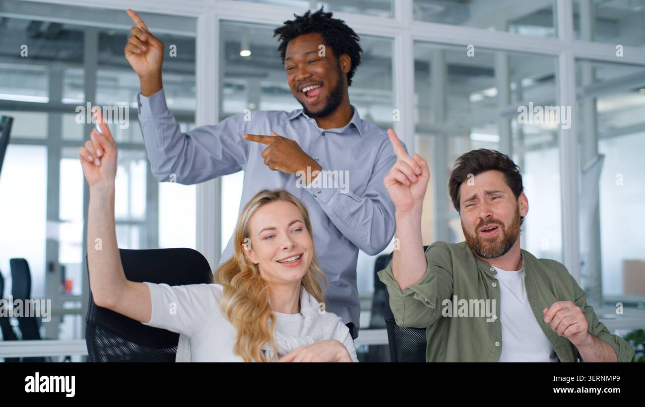 Joyful carefree corporate group business team dancing doing same movement with hands moving having fun clapping palm fooling in office three happy Stock Photo