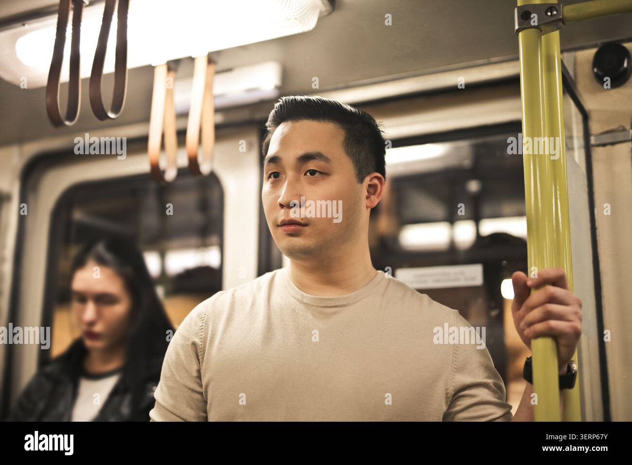 Young Asian man holding a pole on public transportation Stock Photo