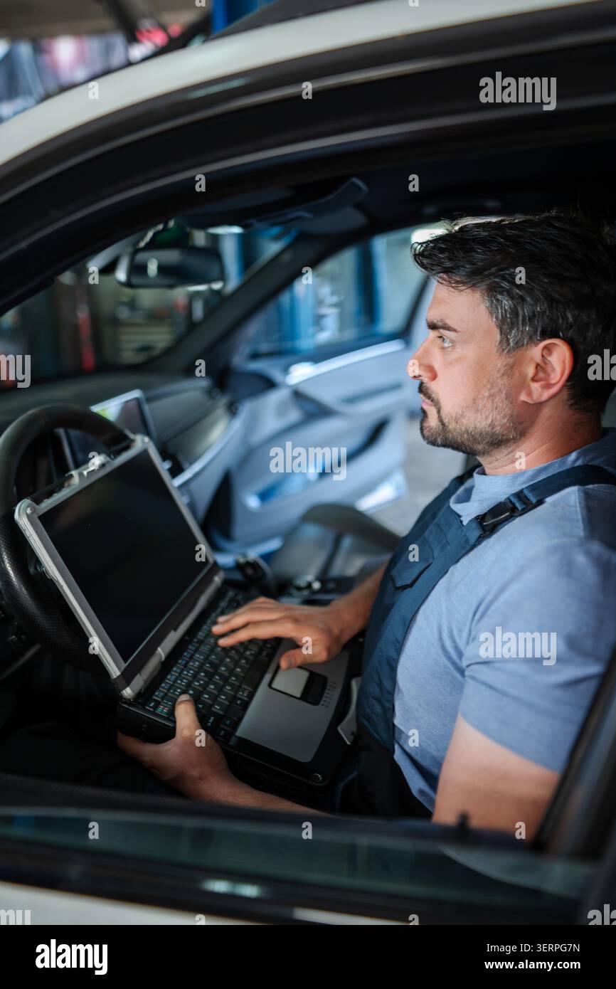 Car mechanic using diagnostic software on a laptop inside a vehicle Stock Photo