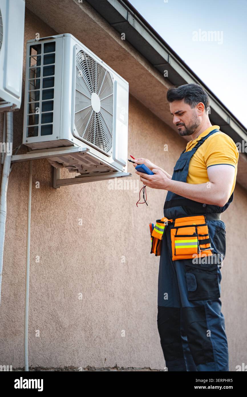 Technician repairing an air conditioner using a digital multimeter Stock Photo