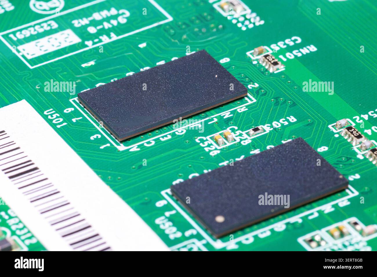 Green circuit board featuring black rectangular microchips, tiny resistors, and printed electronic pathways. Stock Photo