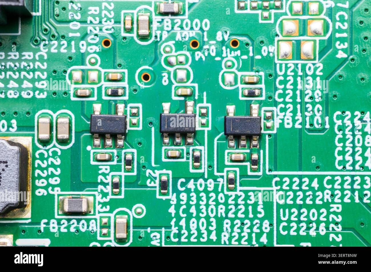 Green circuit board surface with black integrated circuits and numerous tiny electronic components. Stock Photo