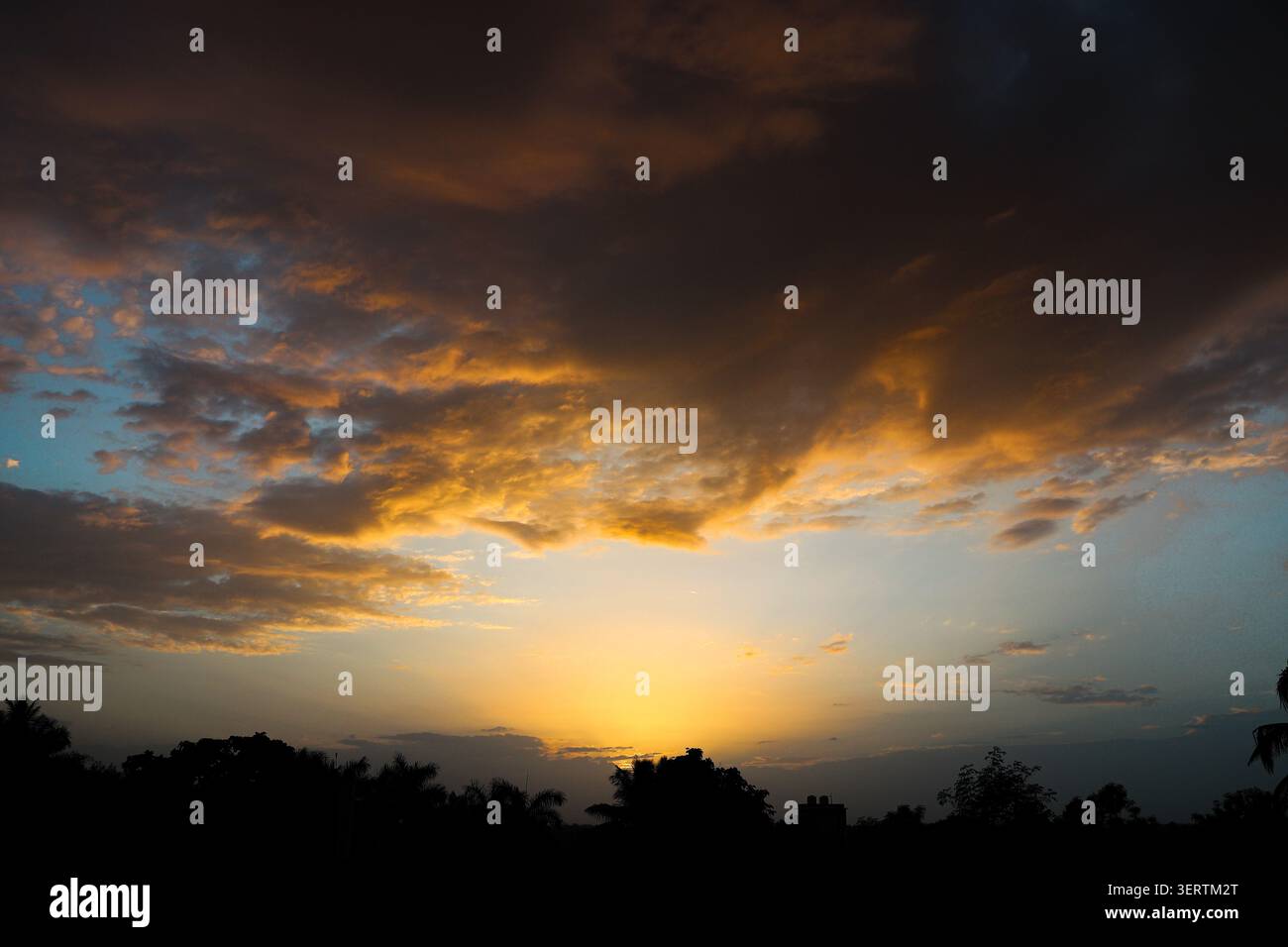 Golden sunset sky with dramatic glowing clouds above dark silhouettes. A breathtaking sunset landscape featuring dramatic orange. Stock Photo