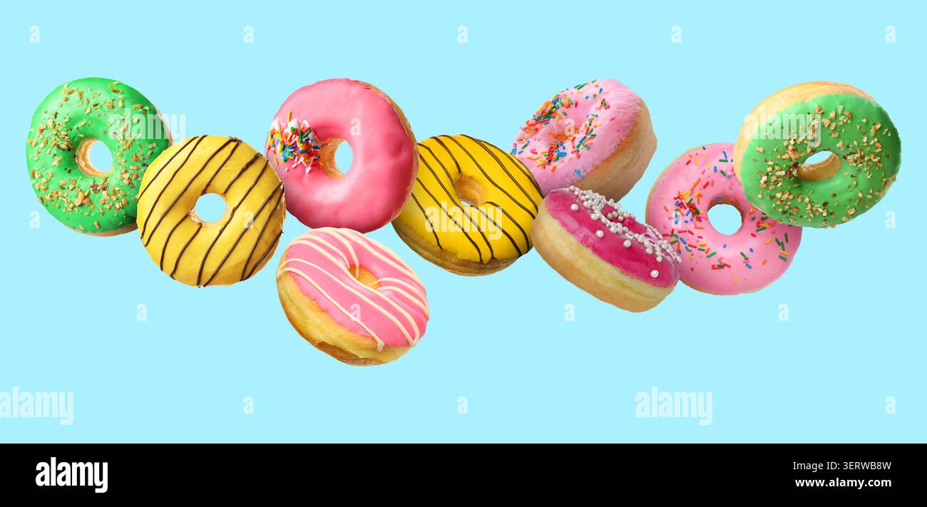 Yummy donuts covered with icing falling on light blue background Stock Photo