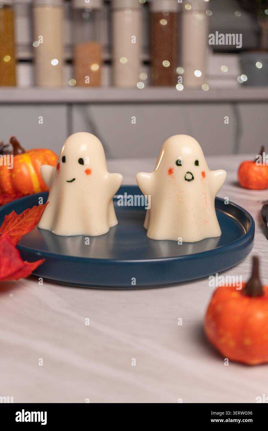 Cute ghost-shaped marshmallow desserts on blue plate with mini pumpkins Stock Photo