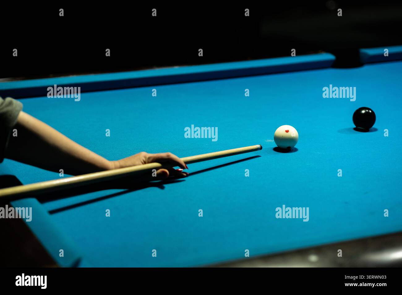 A person is playing pool, aiming at the white ball with a cue stick on a blue table. Stock Photo