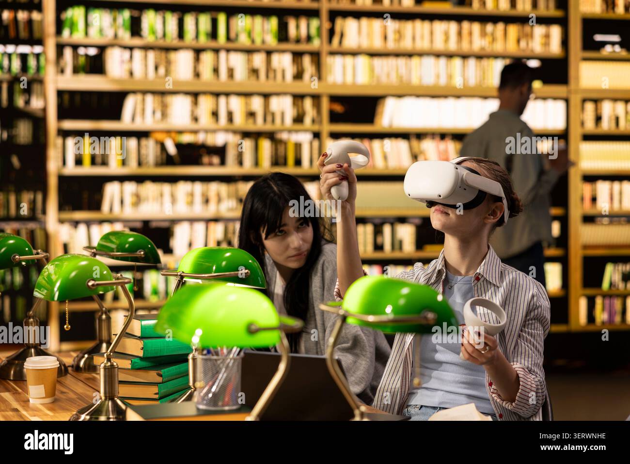 Student using VR device and controller to explore immersive learning at library desk, EdTech and virtual reality used for digital learning and future in education. Modern interactive tools. Stock Photo