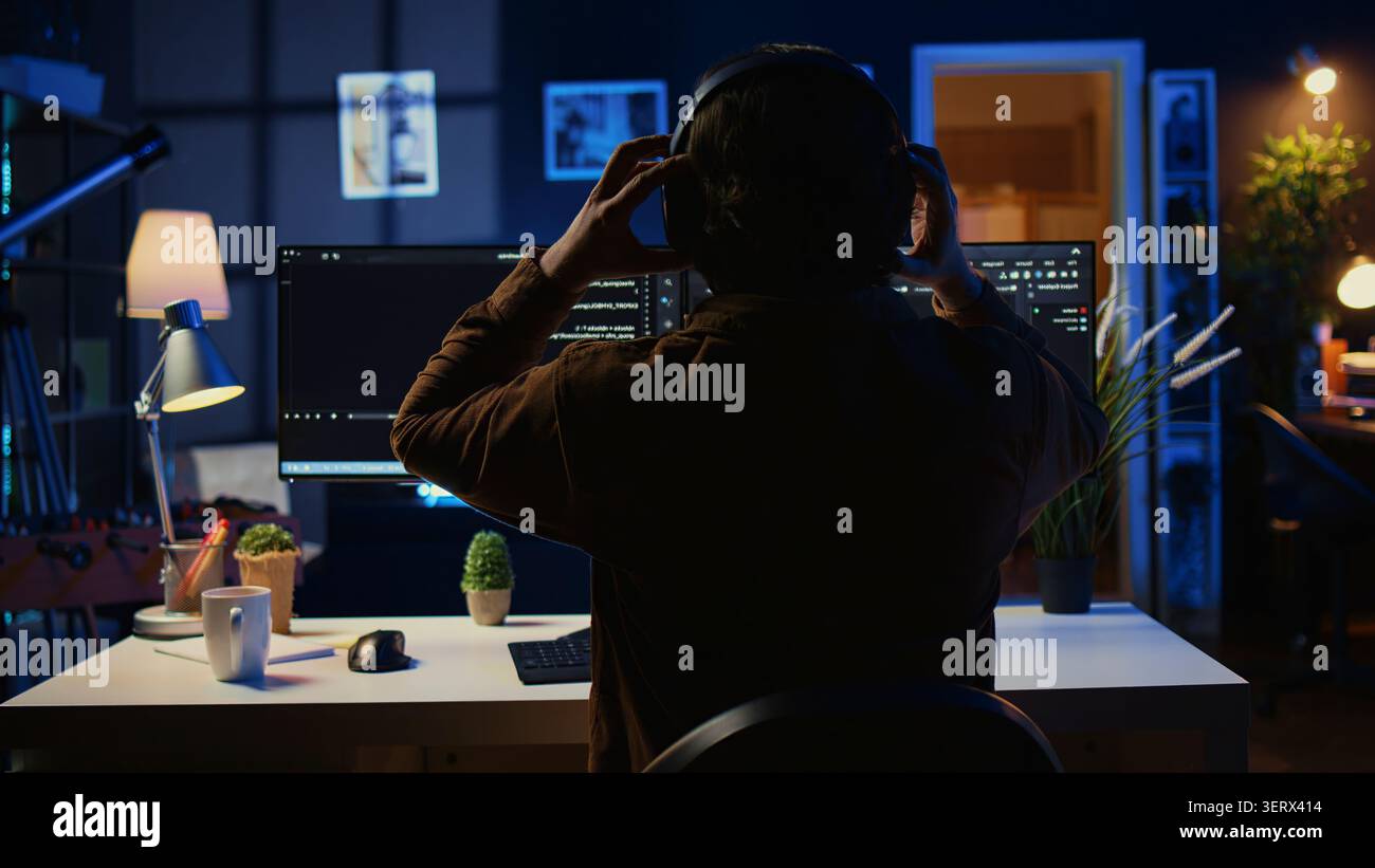 Technician putting headphones on while using coding to fortify firewalls, teleworking for IT company, computer scientist listening music and upgrading binary code scripts in home office. Stock Photo