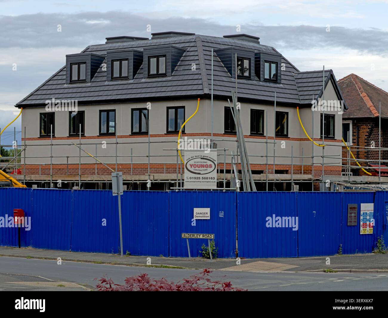 Building under construction on Alderley Road in North West England, UK, with scaffolding and blue site hoardings. Stock Photo