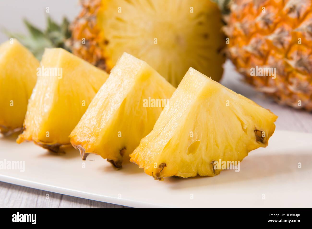Pineapple slices are arranged on a white plate with whole and half pineapples in the background Stock Photo