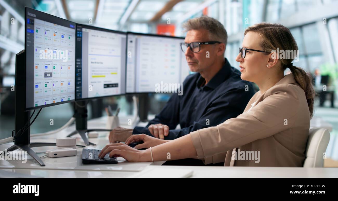 Two Office Workers Analyze Digital Document Workflow System On Computer Screen. Stock Photo