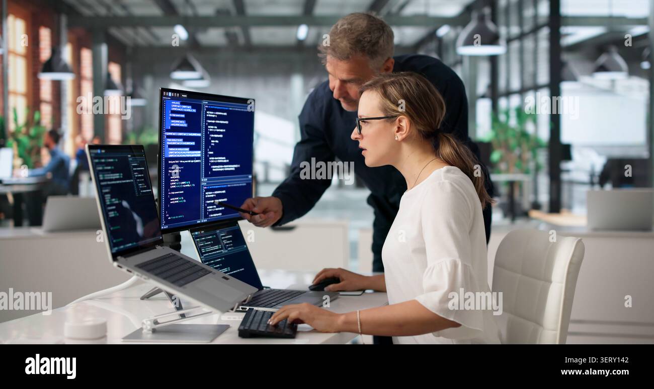 Two Software Engineers Working Together On Secure Code At Office Desk. Stock Photo