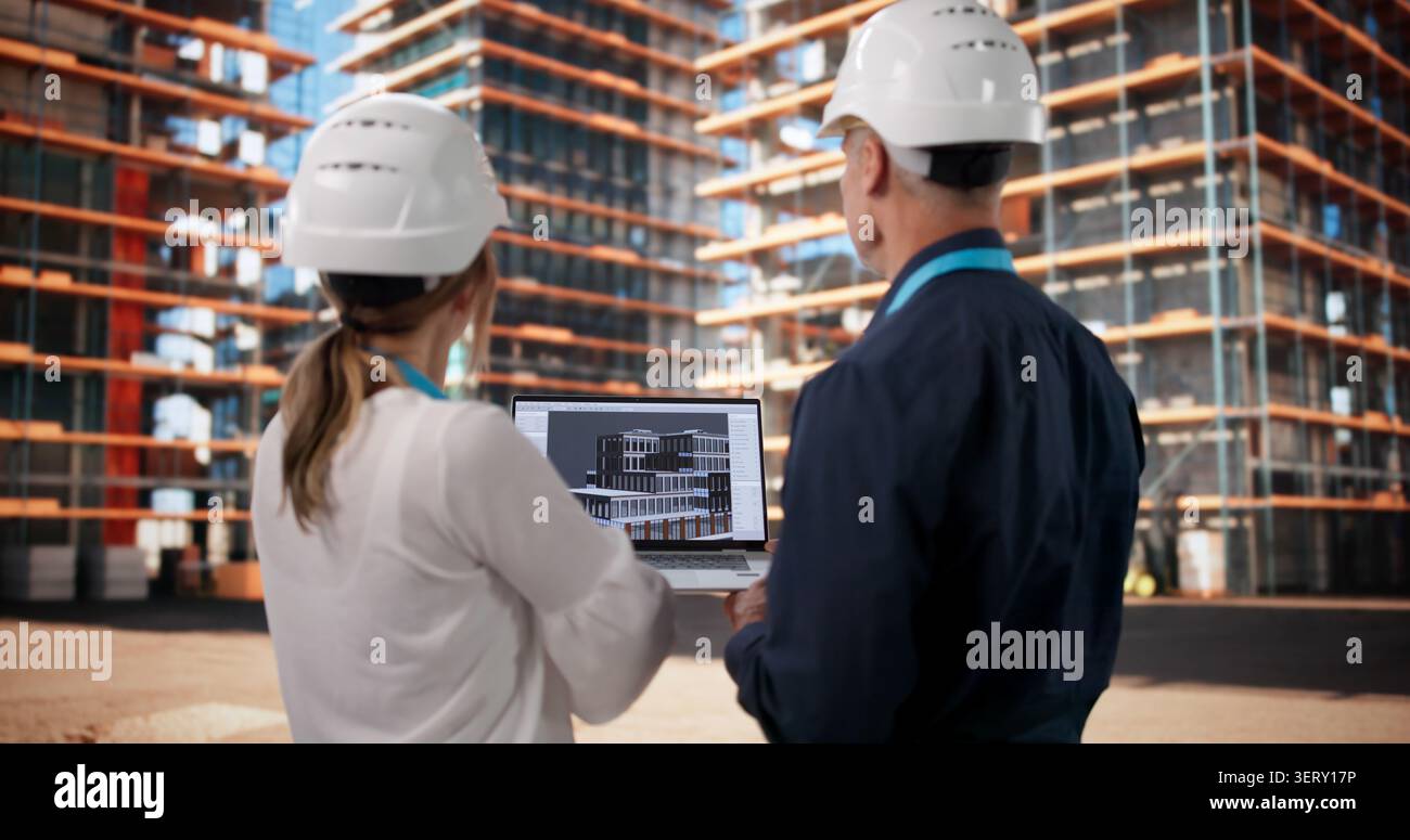 Two Architects And Engineer Discuss 3D BIM Model On Busy Construction Site. Stock Photo