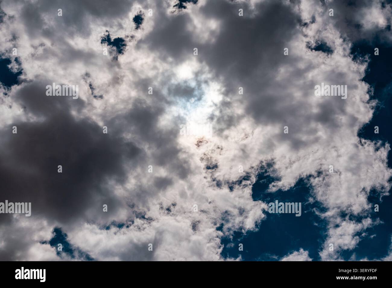 Dramatic sun breaking through dark, heavy storm clouds. Ethereal light of the sun behind dramatic stormy cloud formations. Stock Photo