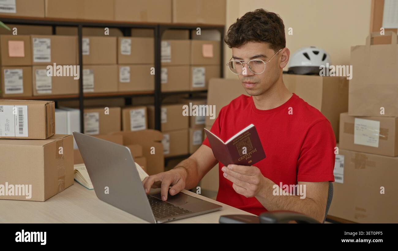Young man in red tshirt holds czech passport and types on laptop while checking packages and boxes in building; entrepreneurship planning focus. Stock Photo