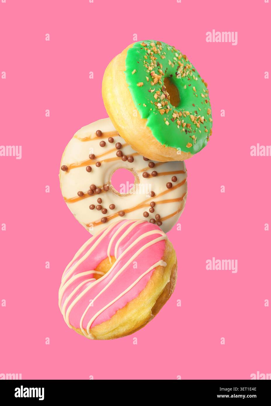 Yummy donuts covered with icing falling on pink background Stock Photo