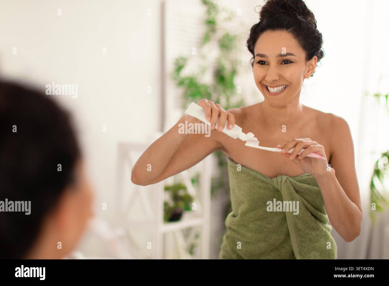 Happy Young Woman Smiling While Brushing Teeth In Bathroom, Home Skincare Routine Stock Photo