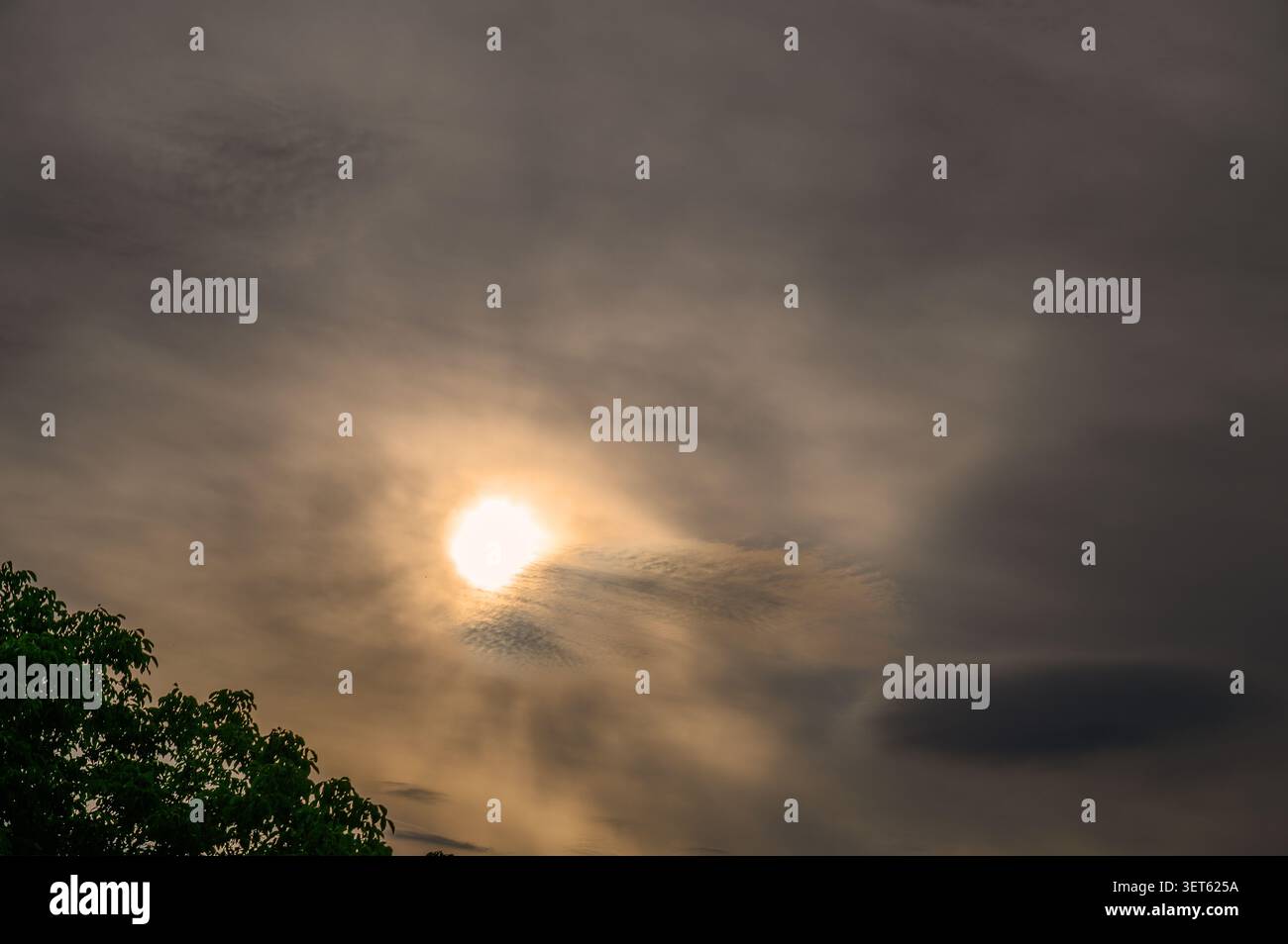 Vibrant sun breaking through dramatic dark clouds in an overcast evening sky. Stock Photo