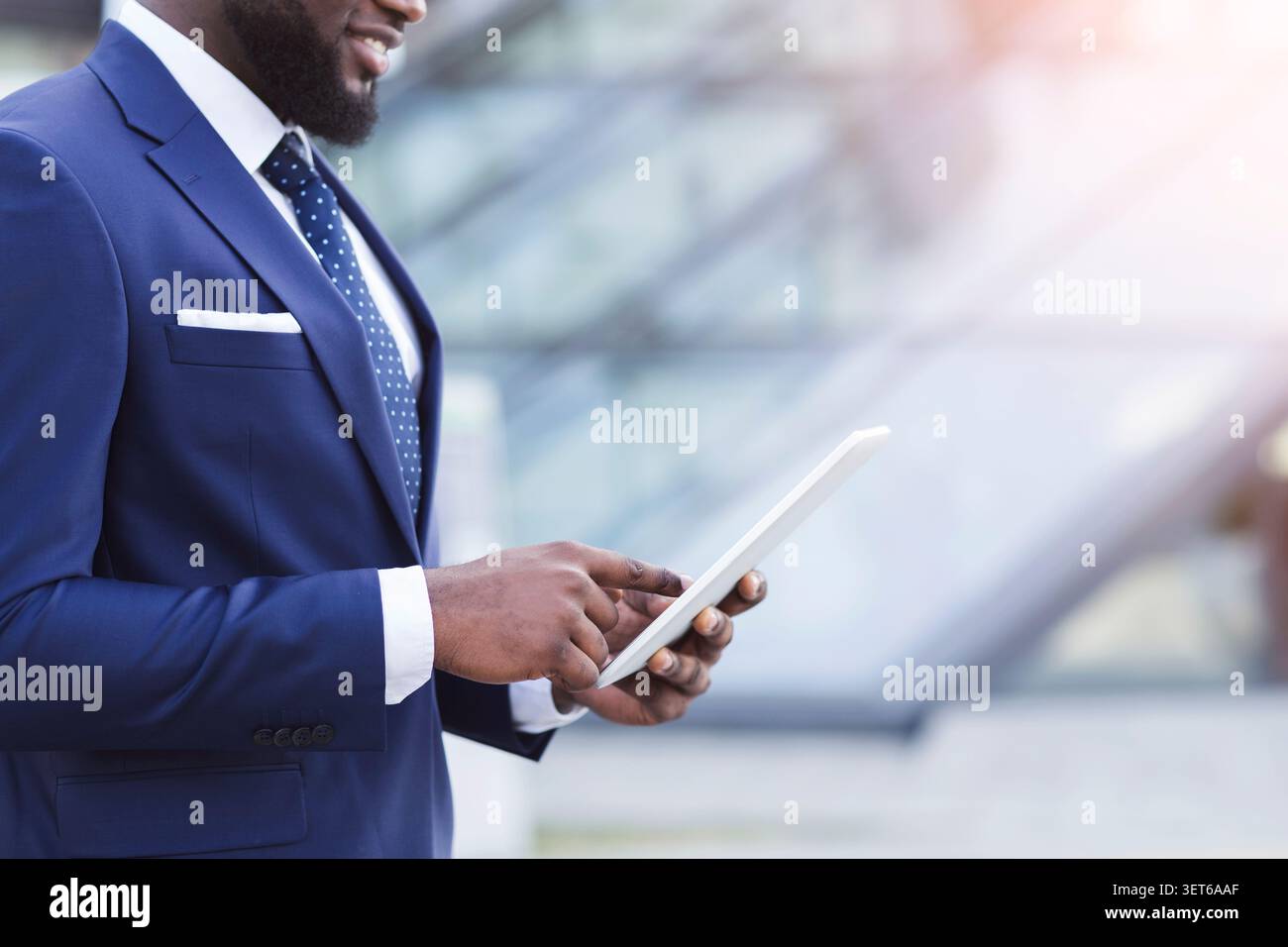 A Man Dressed in a Suit Interacts With a Tablet While Standing in an Urban Area Stock Photo