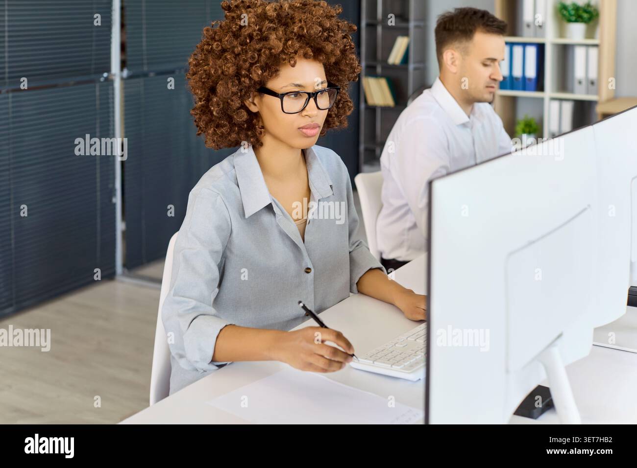 Focused businesswoman working at computer in open office with coworker nearby Stock Photo